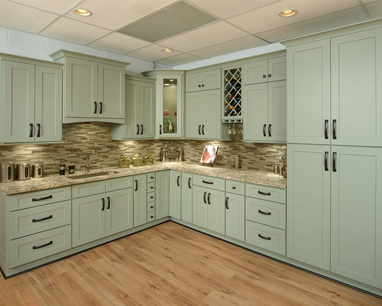 Sage green Shaker kitchen cabinets with black handles, granite countertops, and a stone backsplash.